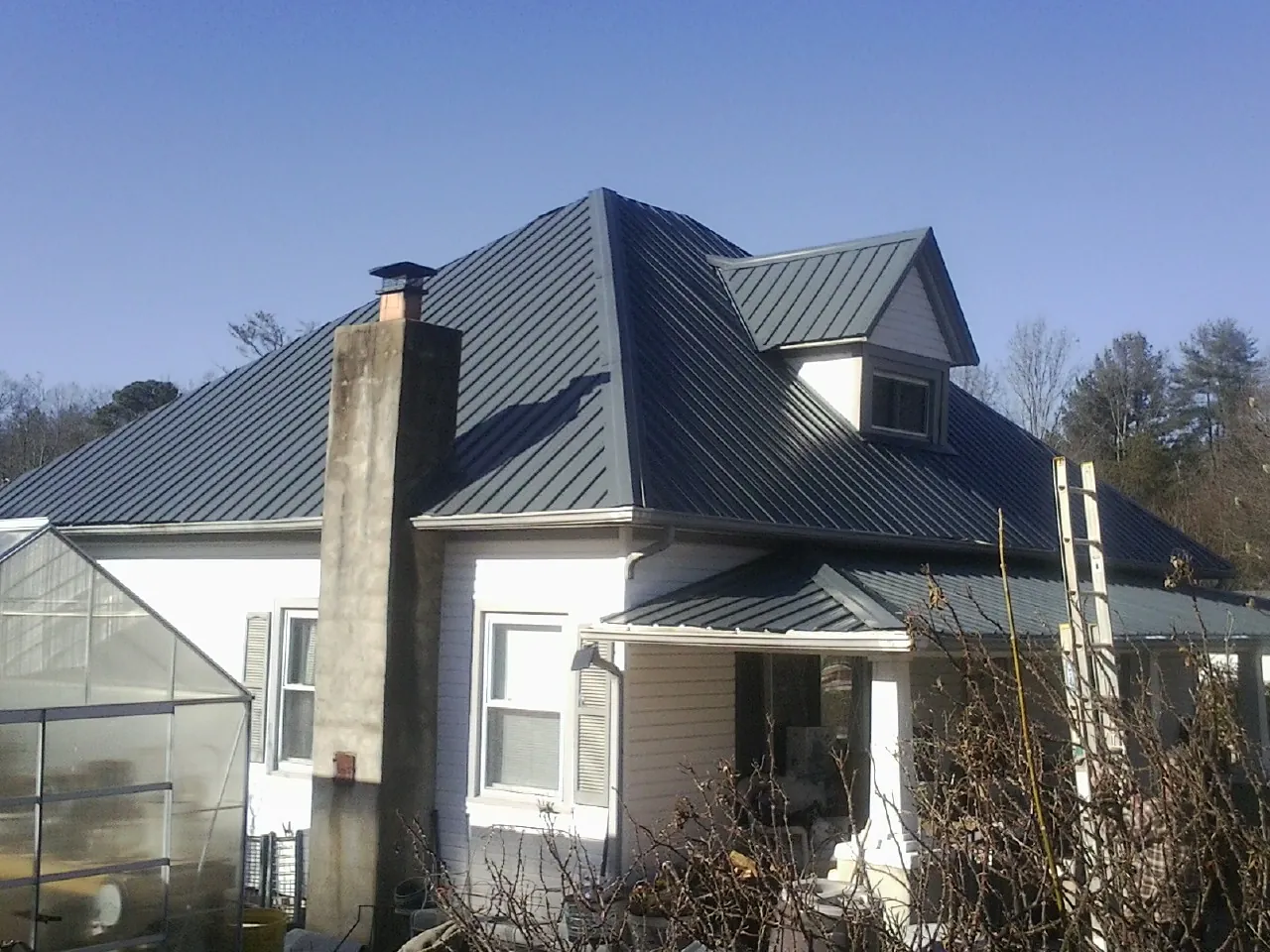 Dark blue standing seam metal roof on a white farmhouse with dormer — Slate & Tile Roof Repair by Roofing Brothers in Cameron