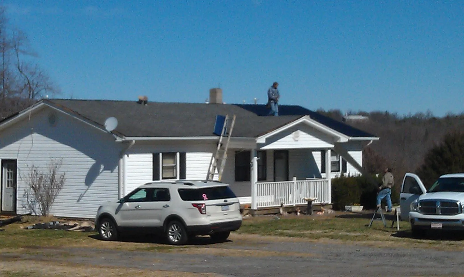 Roofers stripping shingles from a white ranch house roof in Cameron